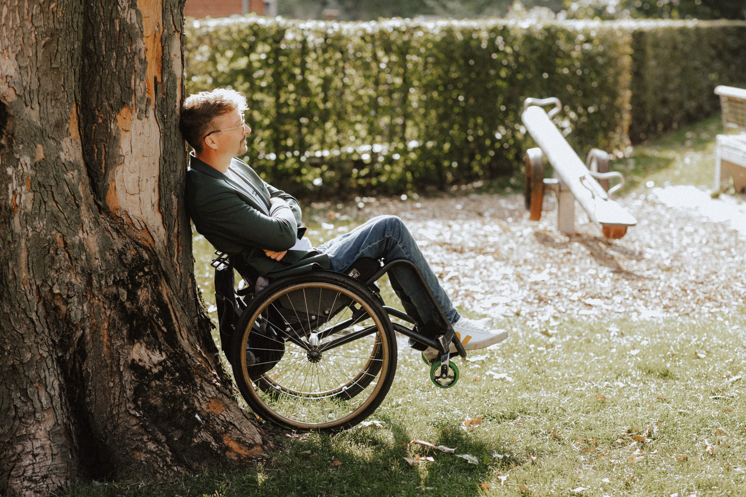 Dennis Sonne lehnt mit seinem Rollstuhl an einem Baum. Er ist dafür leicht nach hinten gekippt – © Schierz&Söhne - Anna Schierz